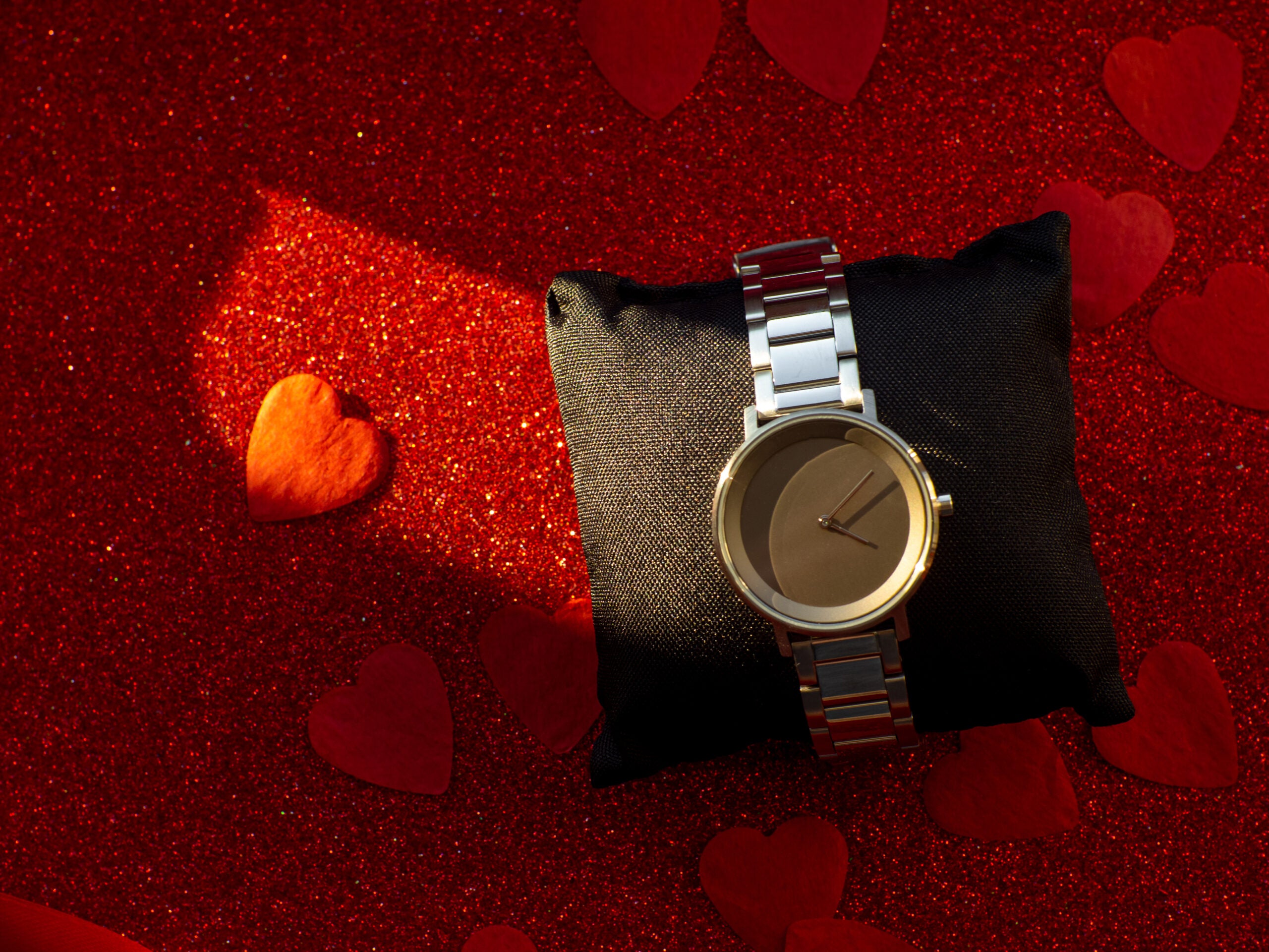 Gift with silver watch is on red heart paper background, top view. Greeting card, present. Valentines day holiday concept. Flat lay with an elegant wristwatch. February 14th.